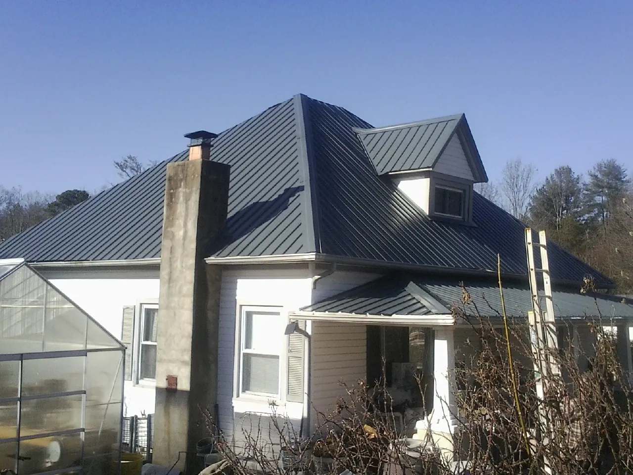 Dark blue standing seam metal roof on a white farmhouse with dormer — Slate & Tile Roof Repair by Roofing Brothers in Nettleton
