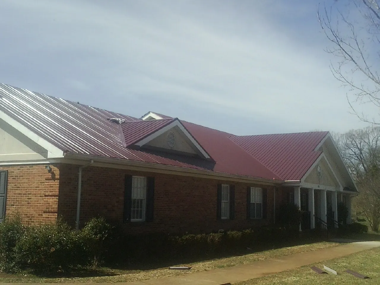Red metal roof with gabled entries on a long brick building, from a Hail Damage Roof Repair job in Nettleton