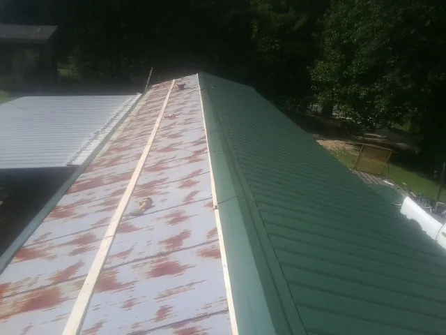Old rusted panels beside newly installed green metal roofing — Wind Damage Roof Repair by Roofing Brothers in Nettleton