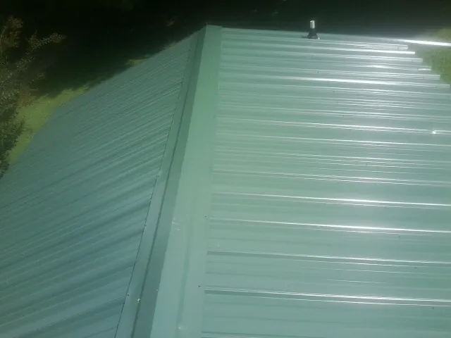 New green metal panels meeting at the ridge of a roof — Flat Roof Repair work by our crew in Nettleton