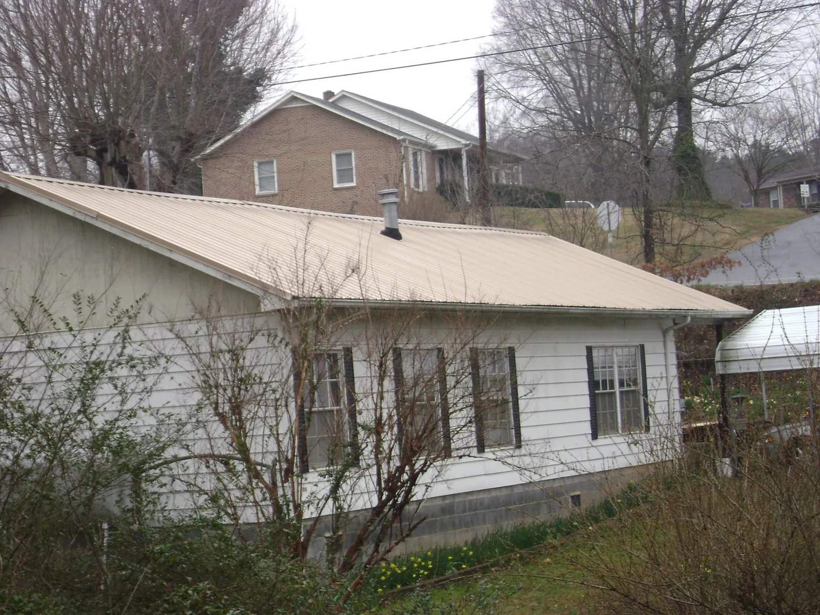 Tan metal roof on a white sided house set into a hillside — Commercial Roofing by Roofing Brothers in Nettleton
