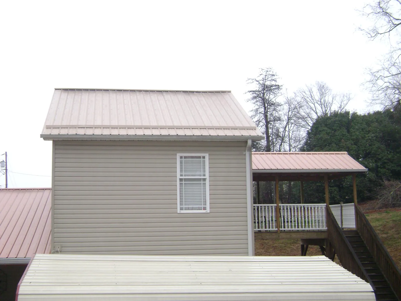 Tan metal roofs on a two story addition and attached porch, from a Roof Replacement job in Nettleton